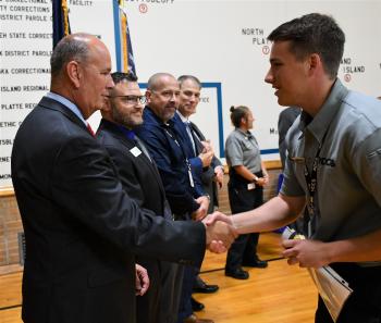 Peru State College Officer Intern Gabriel Stolinski shakes hands with Dir. Frakes upon receiving his certificate and badge